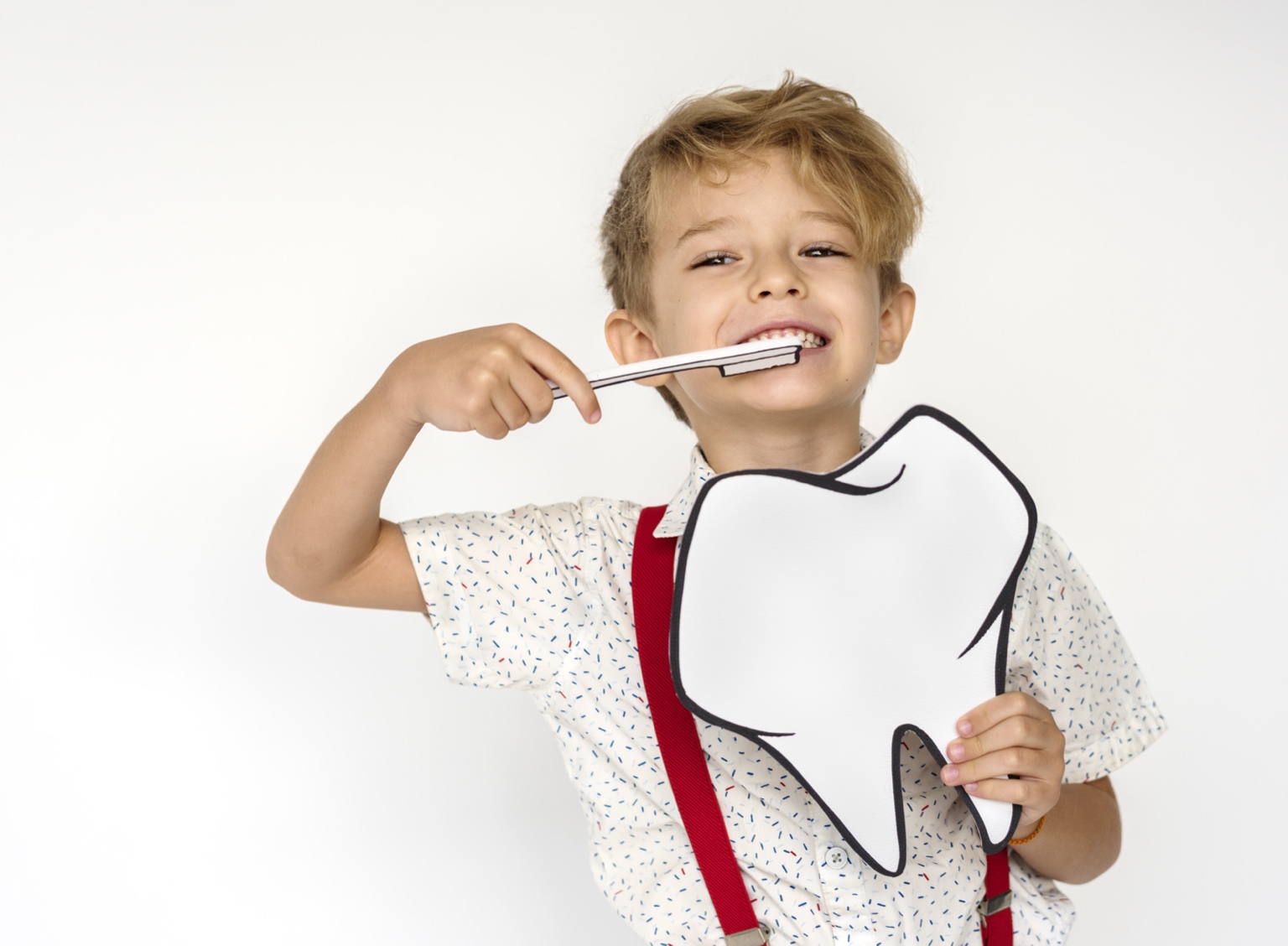 Fotografía ilustrativa de un niño sonriendo con un cepillo y una muela de papel